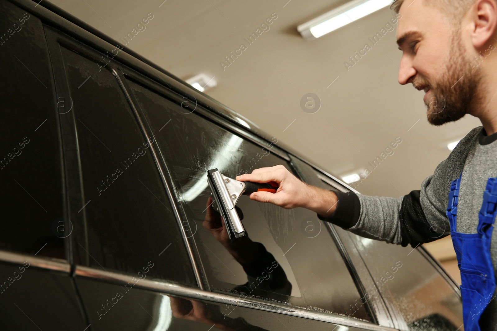 Photo of Skilled worker washing tinted car window in shop