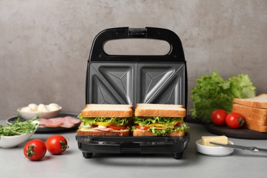 Modern grill maker with tasty sandwiches on light grey table
