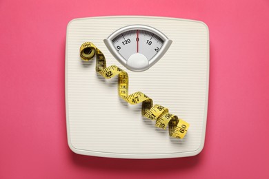 Photo of Weigh scales and measuring tape on pink background, top view. Overweight concept