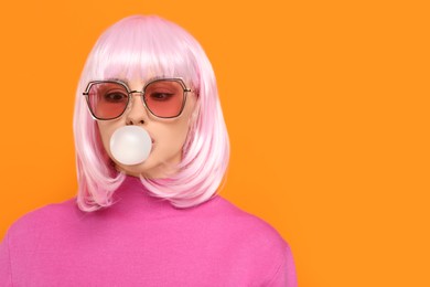 Photo of Beautiful woman in sunglasses blowing bubble gum on orange background, space for text