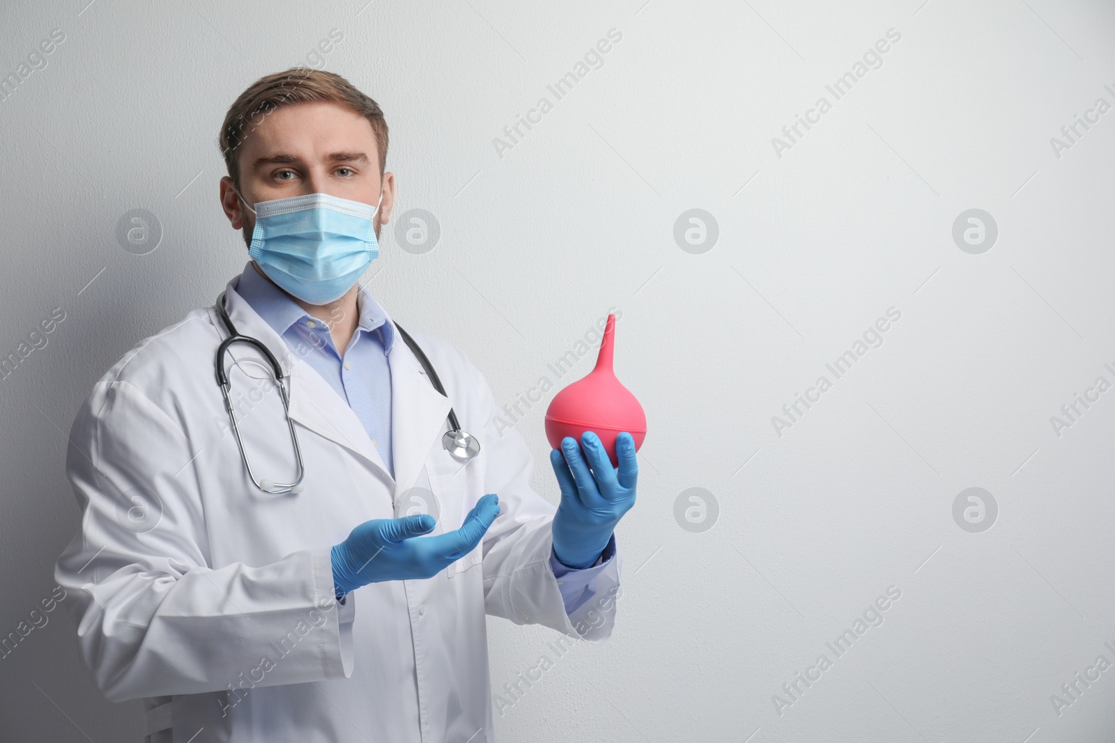 Photo of Doctor holding rubber enema on grey background. Space for text