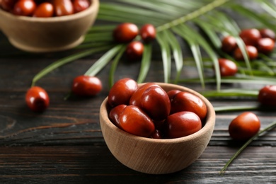Photo of Palm oil fruits in bowl on black wooden table, closeup