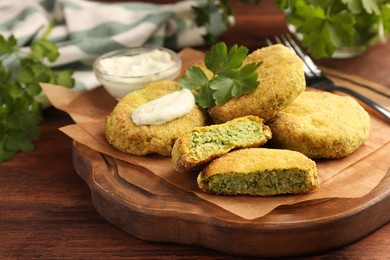 Photo of Tasty vegan cutlets served with sauce and parsley on wooden table, closeup
