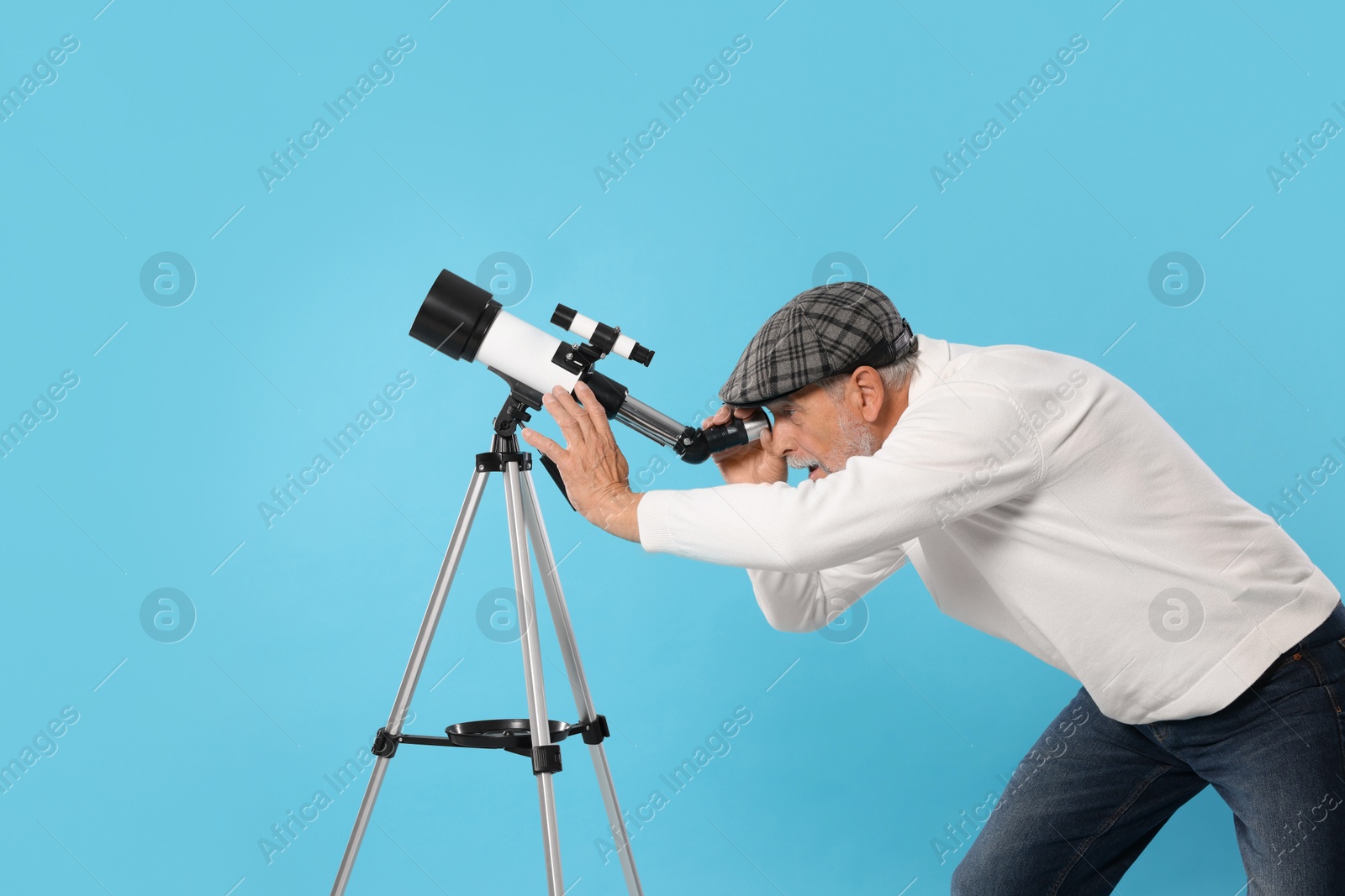 Photo of Senior astronomer looking at stars through telescope on light blue background