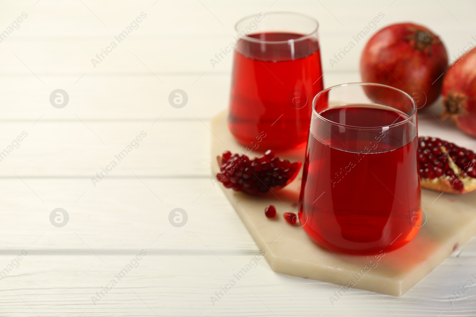 Photo of Tasty pomegranate juice in glasses and fresh fruits on white wooden table, closeup. Space for text