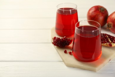 Photo of Tasty pomegranate juice in glasses and fresh fruits on white wooden table, closeup. Space for text