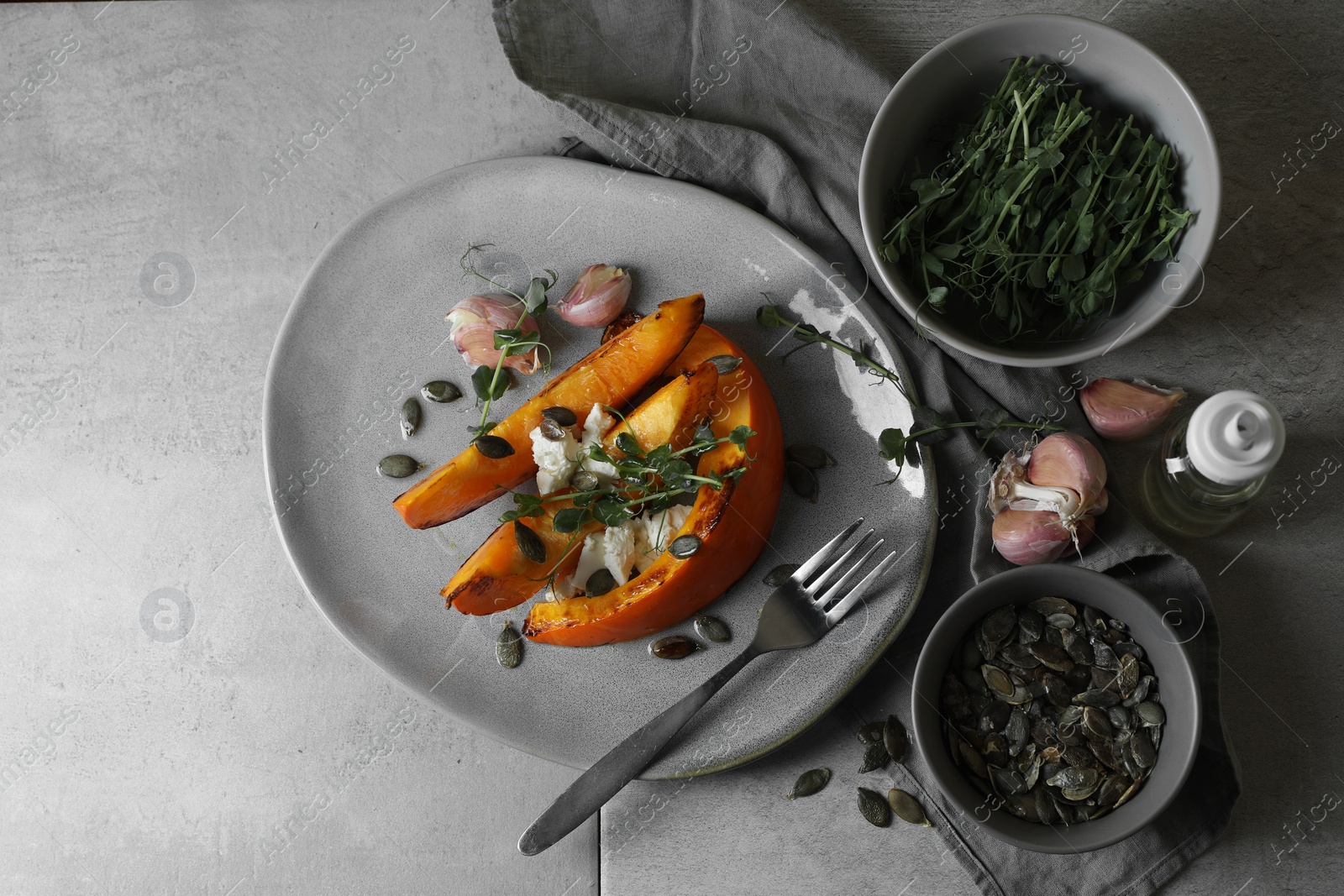 Photo of Baked pumpkin slices served with cheese, microgreens, seeds and garlic on light table, flat lay