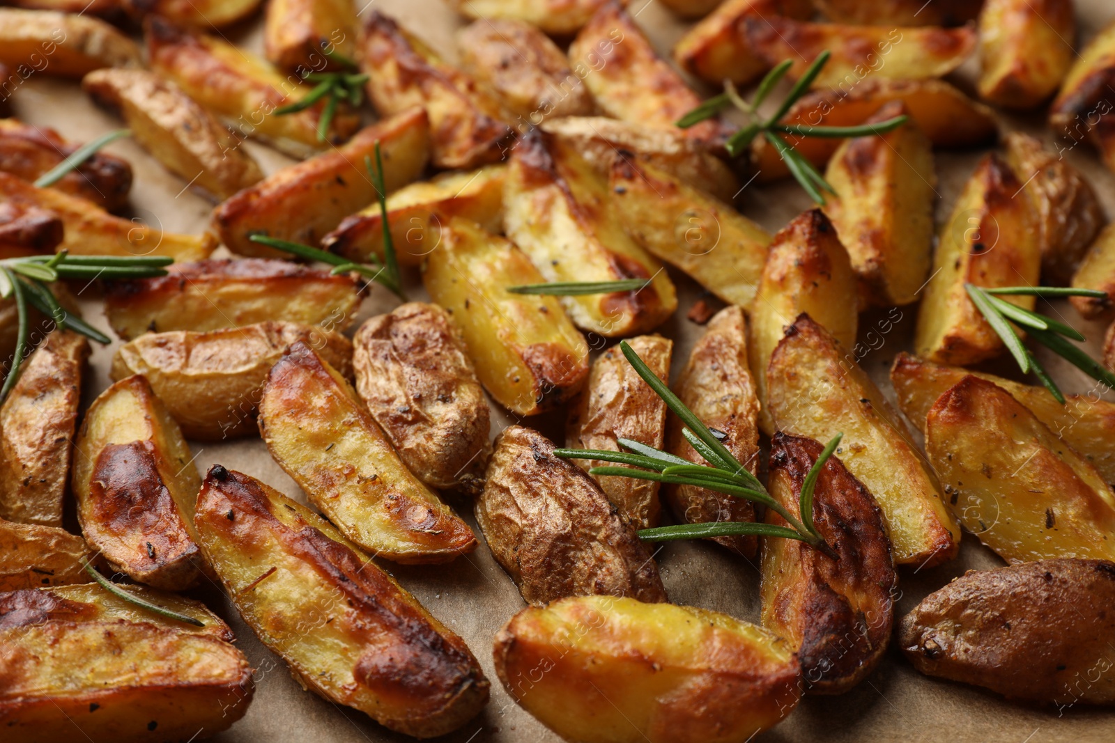 Photo of Tasty baked potato and aromatic rosemary on parchment paper, closeup