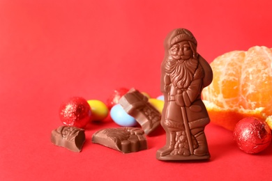 Photo of Chocolate Santa Claus candies, sweets and tangerine on red background, space for text