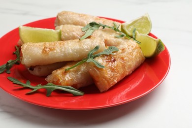 Photo of Plate with tasty fried spring rolls, arugula and lime on white table, closeup
