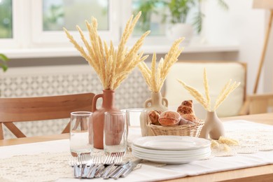 Photo of Clean dishes, dry spikes and fresh pastries on table in stylish dining room