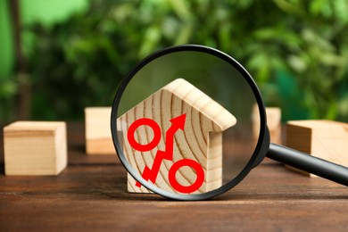 Image of Mortgage rate rising illustrated by percent sign with upward arrow. House model on wooden table, view through magnifying glass