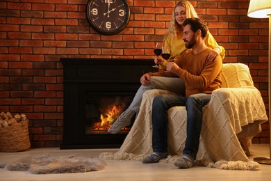 Lovely couple with glasses of wine spending time together near fireplace at home
