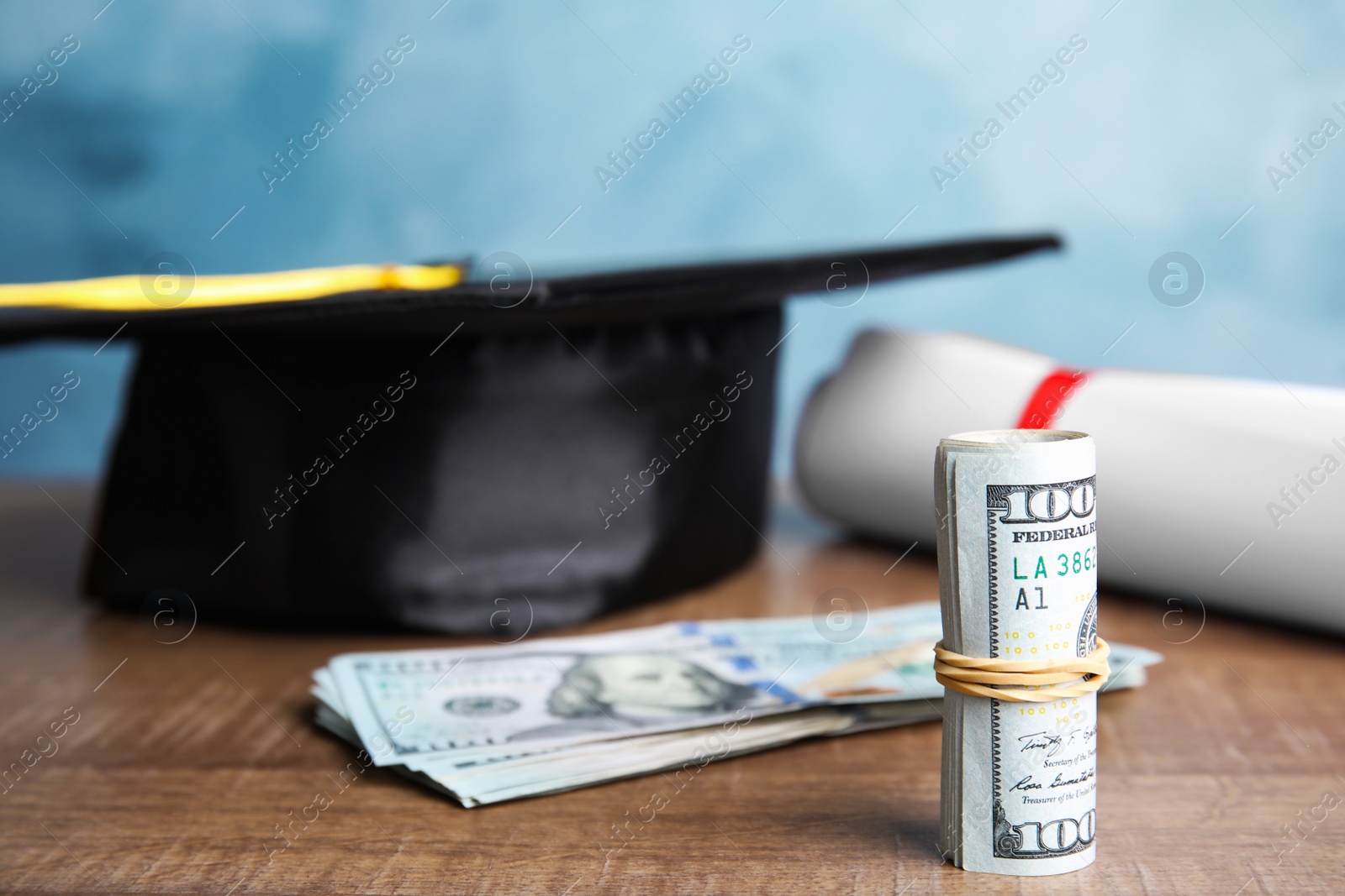 Photo of Dollar banknotes and student graduation hat on wooden table against blue background. Tuition fees concept