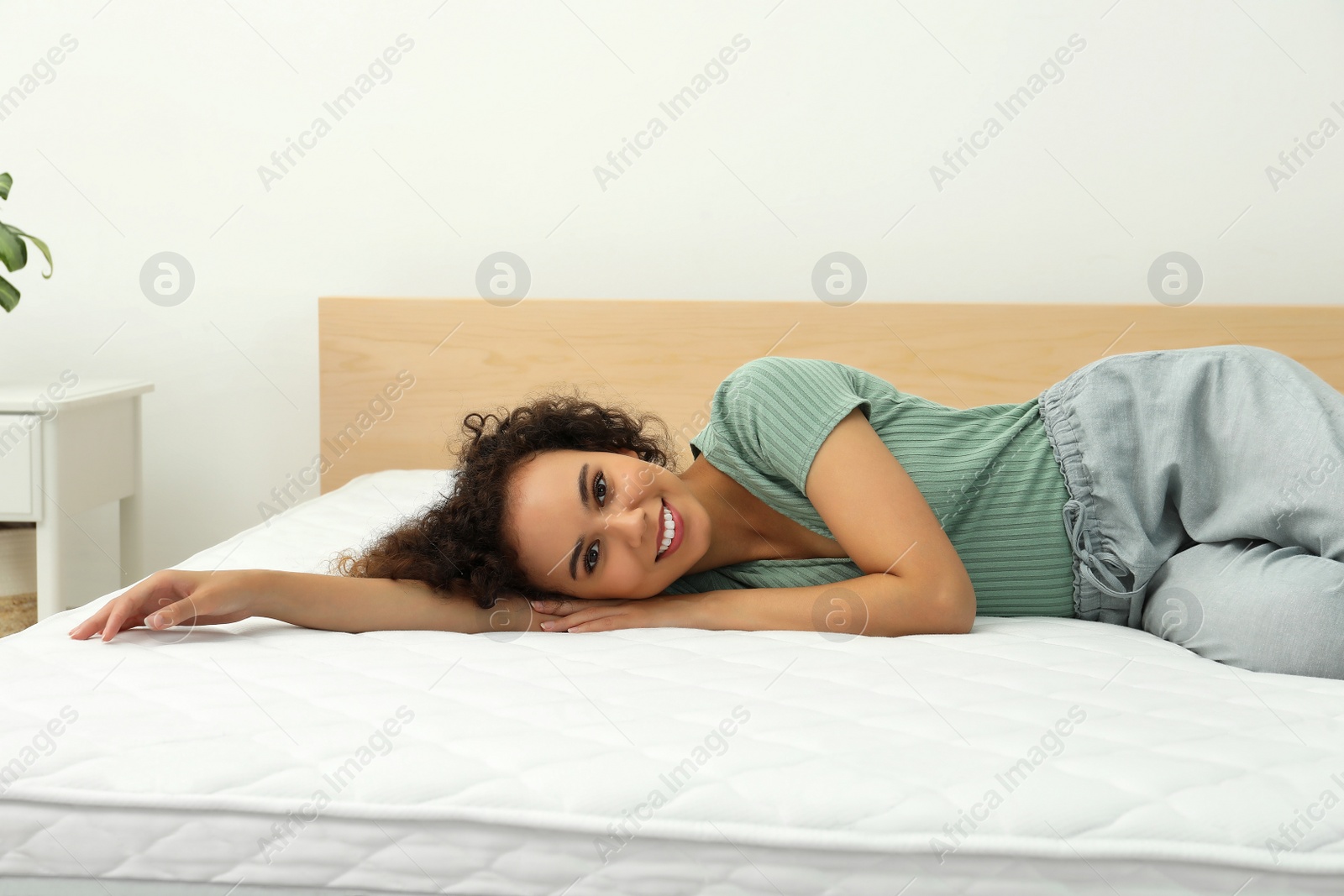 Photo of Happy young African American woman on bed with comfortable mattress at home