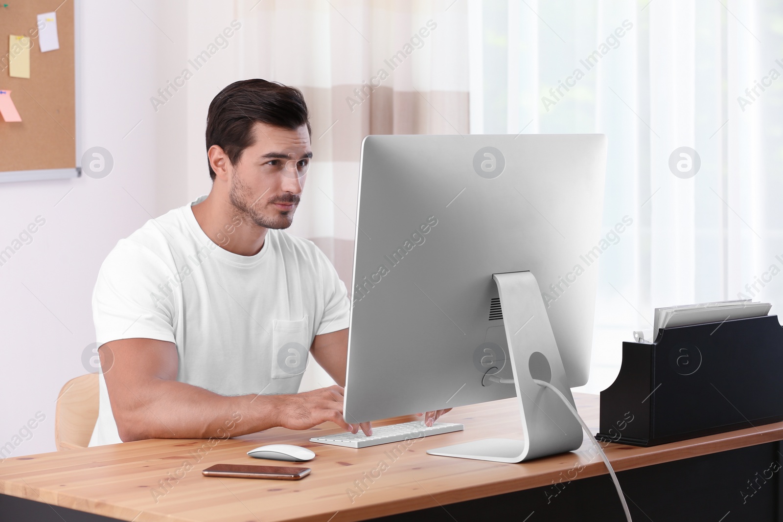 Photo of Handsome young man working with computer at table in office