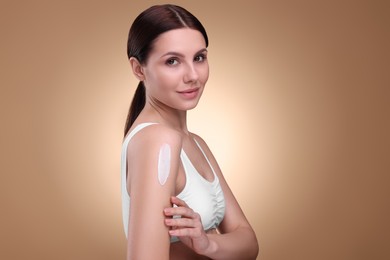 Photo of Beautiful woman with smear of body cream on her shoulder against light brown background