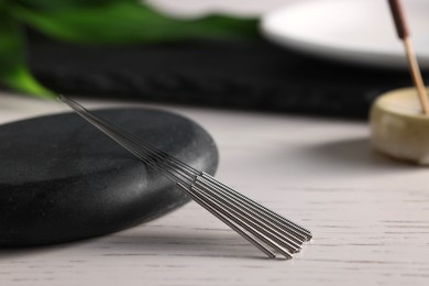 Photo of Acupuncture needles and spa stone on white wooden table, closeup. Space for text