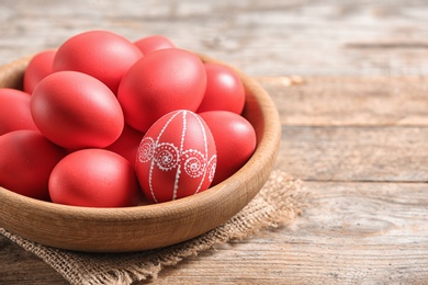 Photo of Wooden bowl with red painted Easter eggs on table, space for text