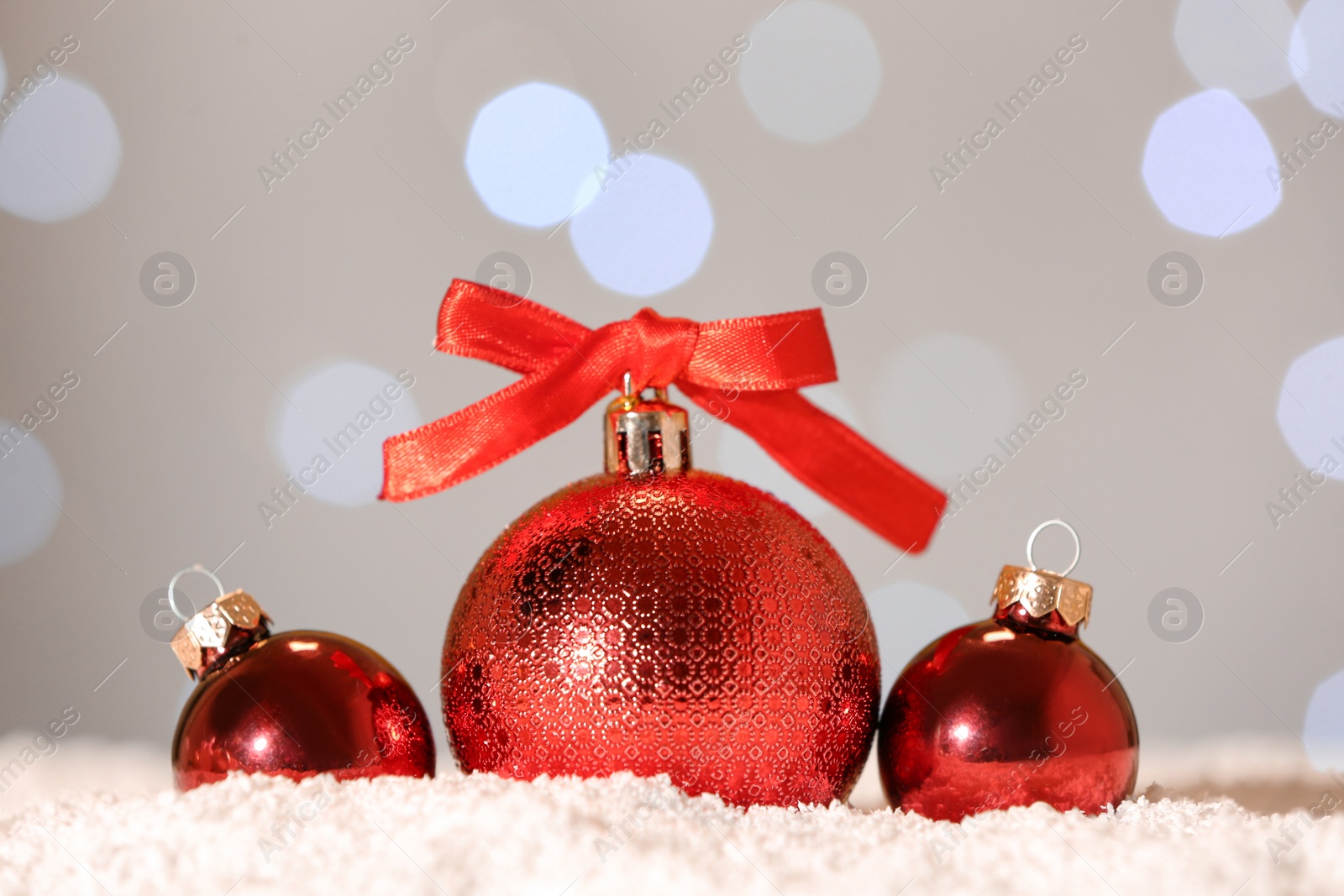 Photo of Beautiful red Christmas balls on snow against blurred festive lights