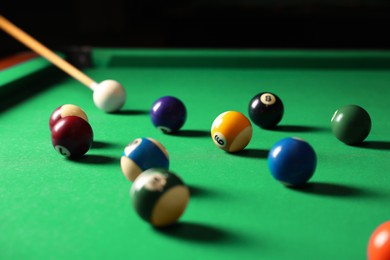 Many colorful billiard balls and cue on green table indoors