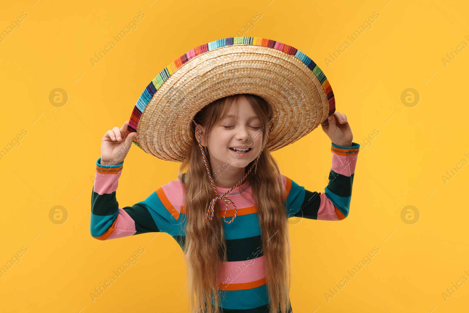 Photo of Cute girl in Mexican sombrero hat on orange background