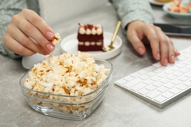 Photo of Bad habits. Woman eating popcorn while working on computer at light grey table, closeup