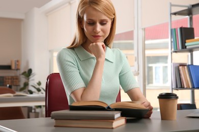 Young woman reading book at table in library