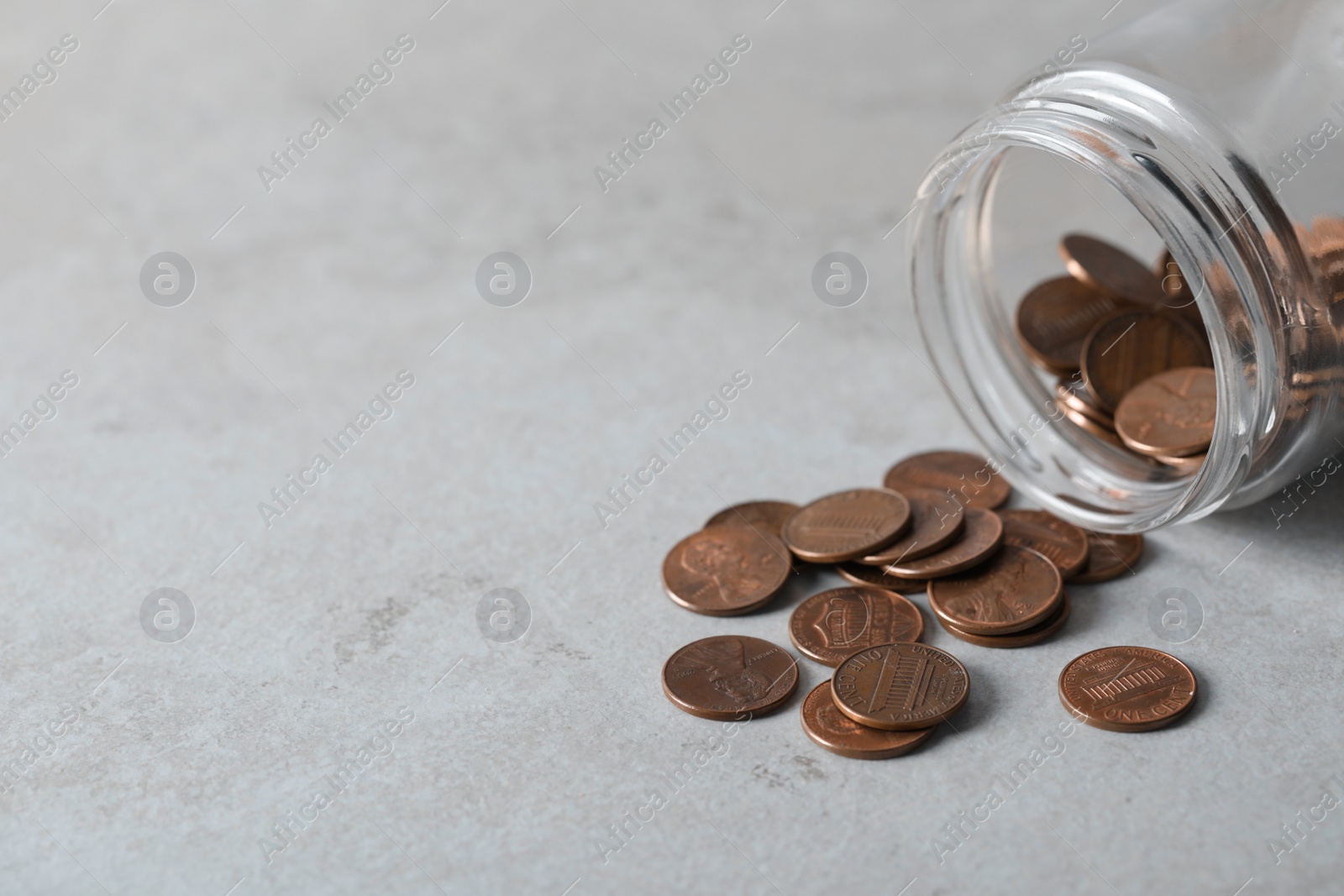 Photo of Glass jar with coins on light grey table, closeup. Space for text