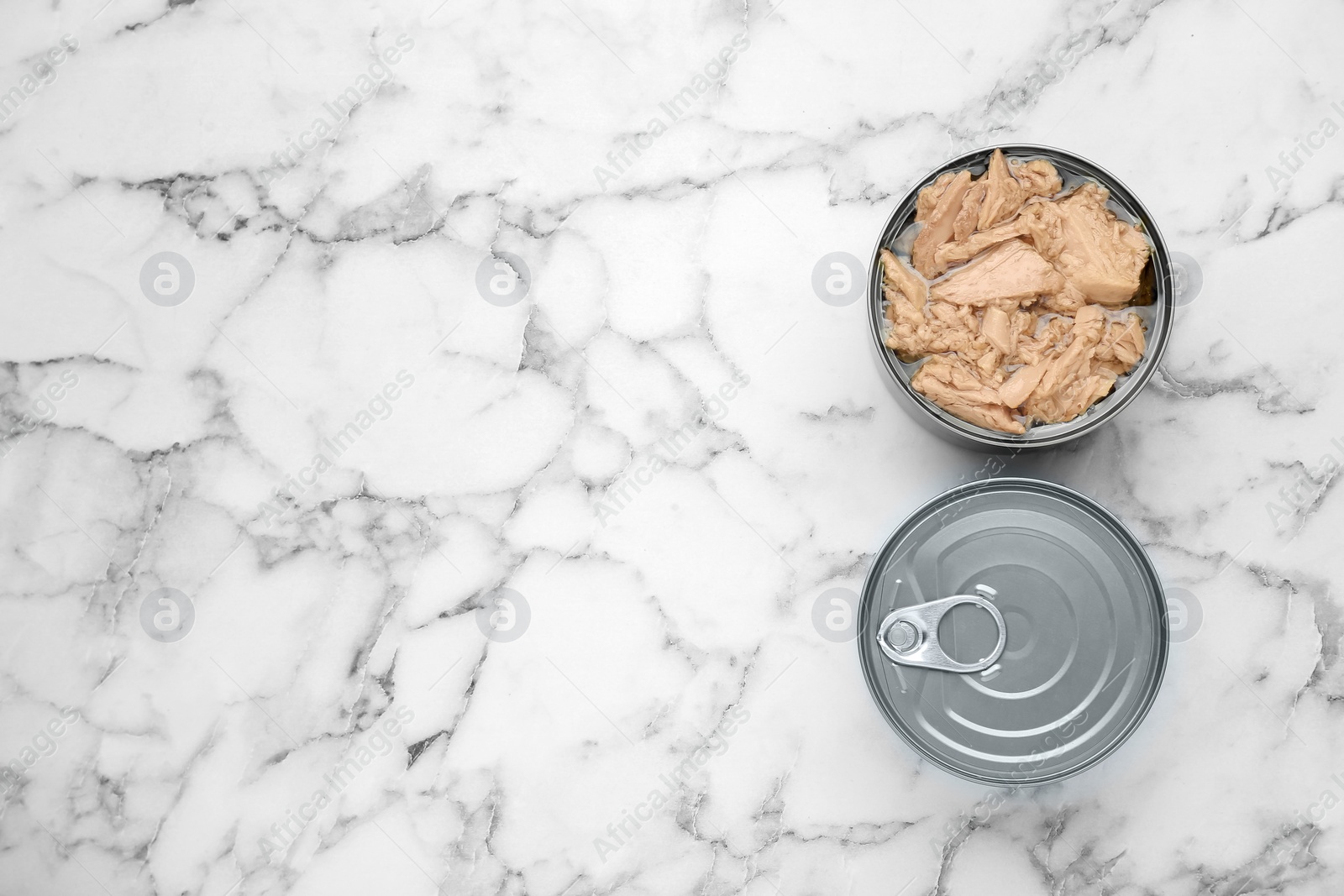 Photo of Tin cans with canned tuna on white marble table, flat lay. Space for text