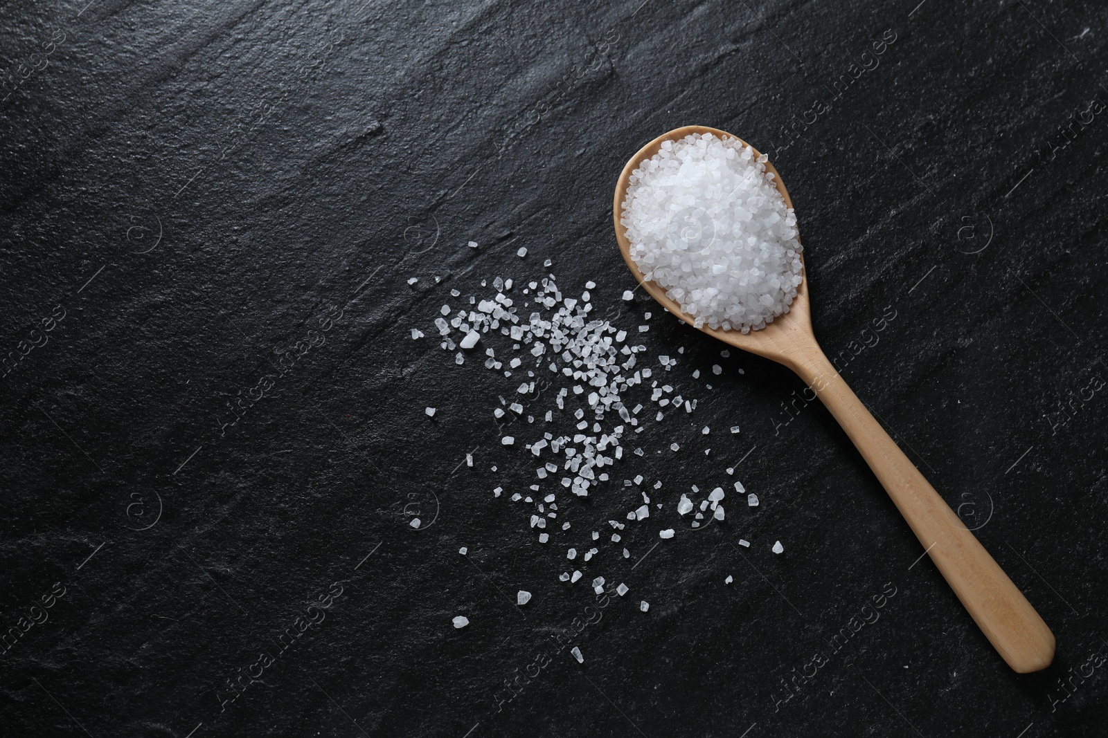 Photo of Organic white salt and spoon on black table, top view. Space for text