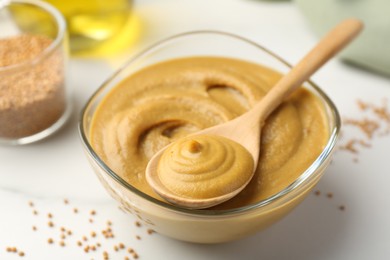 Spoon and glass bowl with tasty mustard sauce on white table, closeup