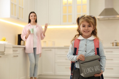 Photo of Little girl with lunch bag and mother in kitchen. Getting ready for school