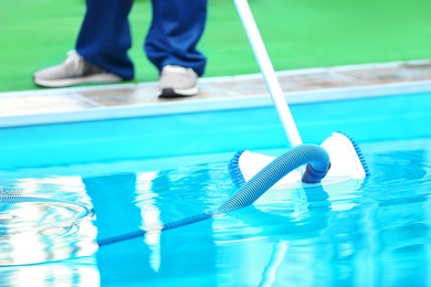 Photo of Male worker cleaning outdoor pool with underwater vacuum