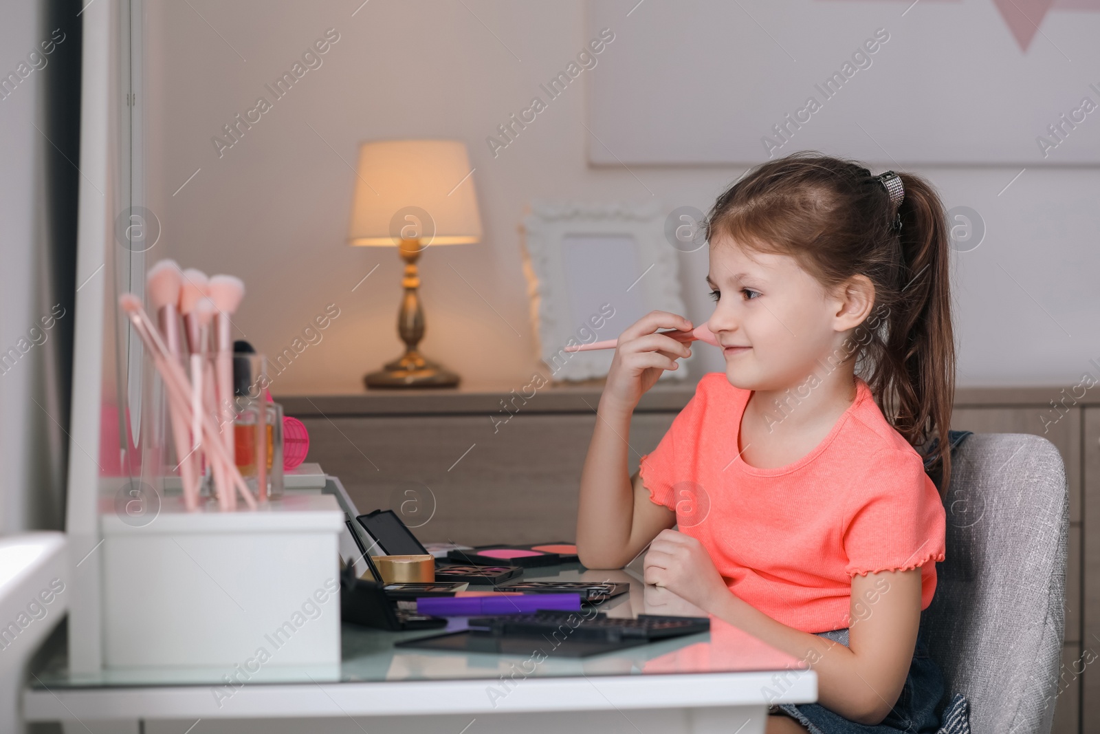 Photo of Adorable little girl applying makeup at dressing table indoors