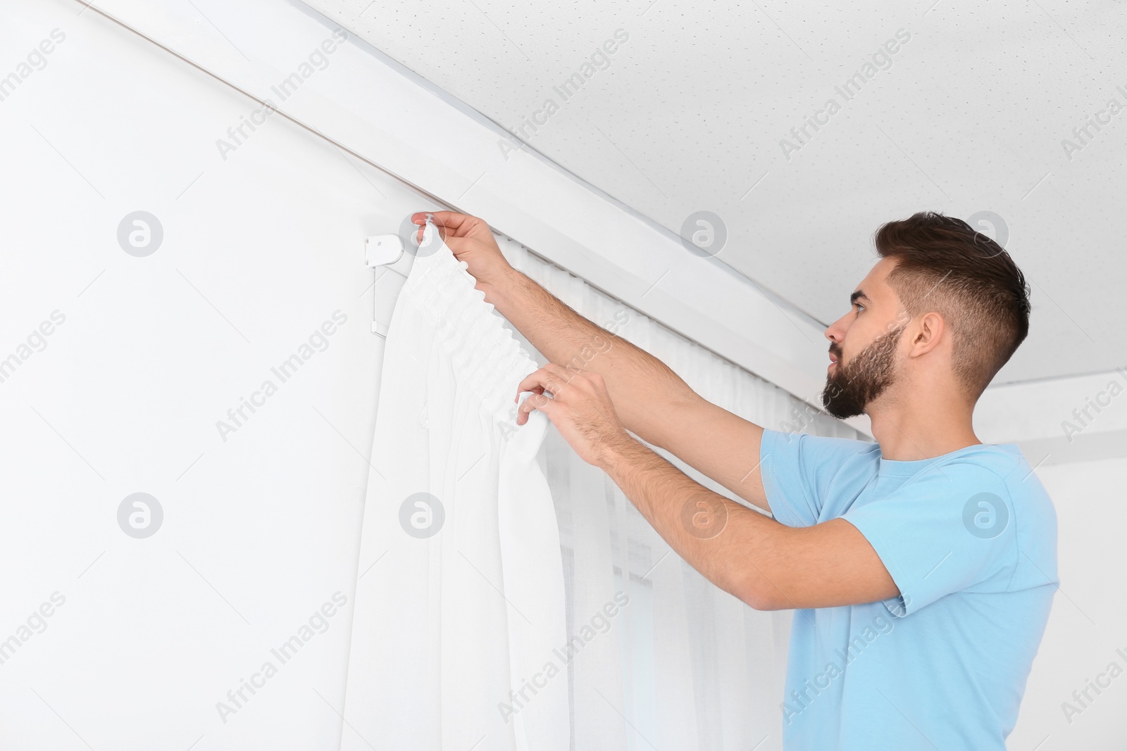 Photo of Young handsome man hanging window curtain in room