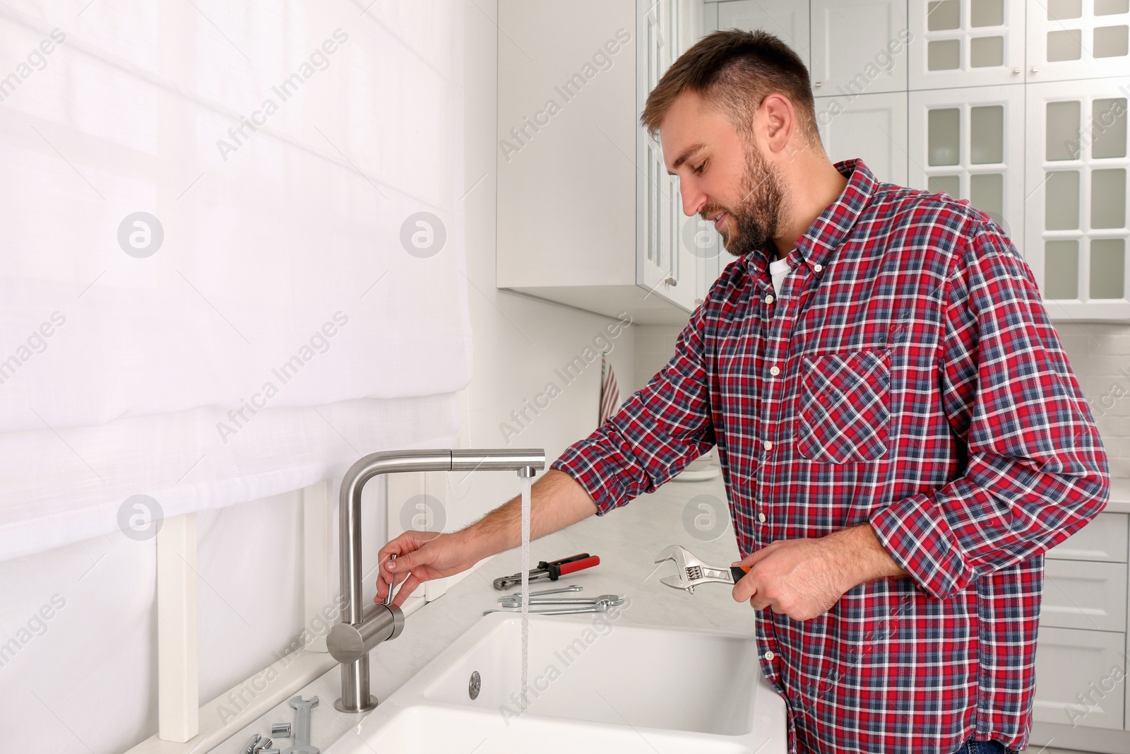 Photo of Man checking water flow from tap in kitchen. Repair and installation