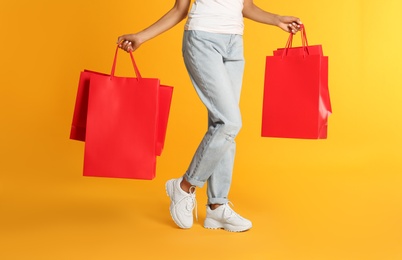 Photo of Young woman with paper shopping bags on yellow background, closeup