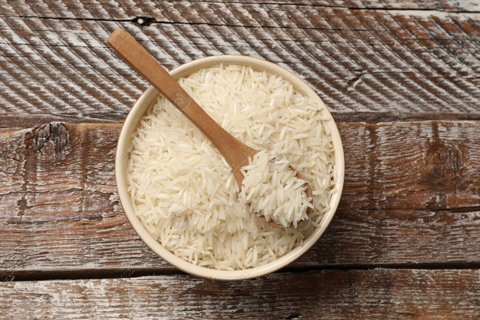 Photo of Raw basmati rice and spoon in bowl on wooden table, top view