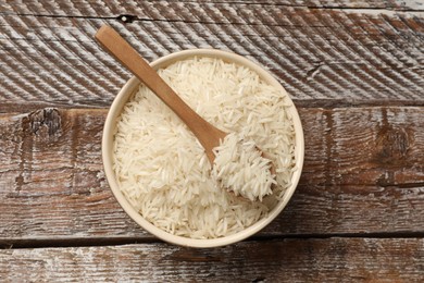 Photo of Raw basmati rice and spoon in bowl on wooden table, top view