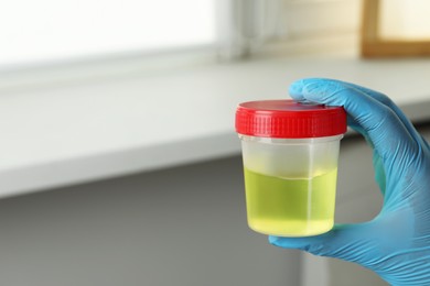 Photo of Doctor holding container with urine sample for analysis indoors, closeup. Space for text