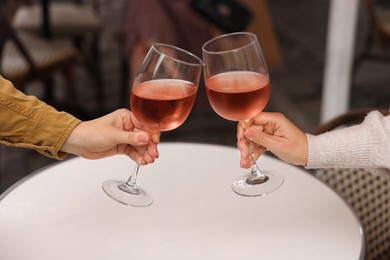 Photo of Women clinking glasses with rose wine at white table in outdoor cafe, closeup