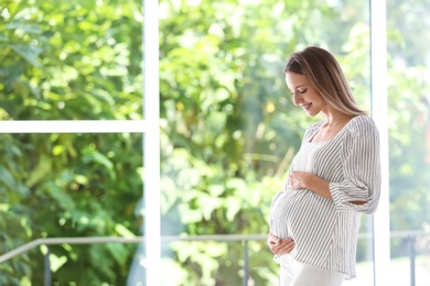 Happy pregnant woman standing near window at home