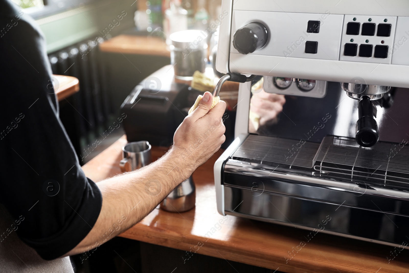 Photo of Barista cleaning coffee machine steam wand with rag on bar counter, closeup