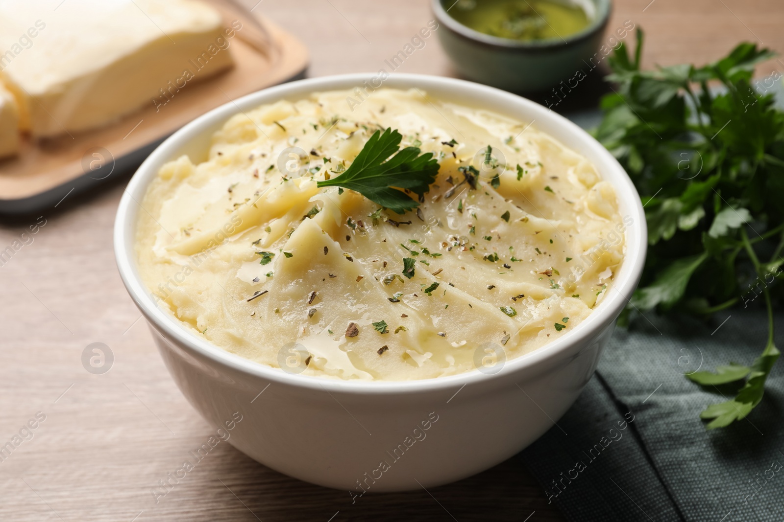 Photo of Bowl of delicious mashed potato with parsley on wooden table, closeup