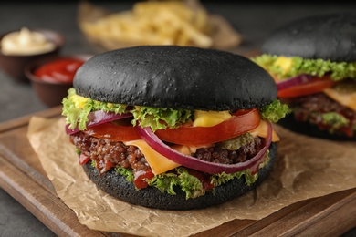 Board with black burgers on table, closeup