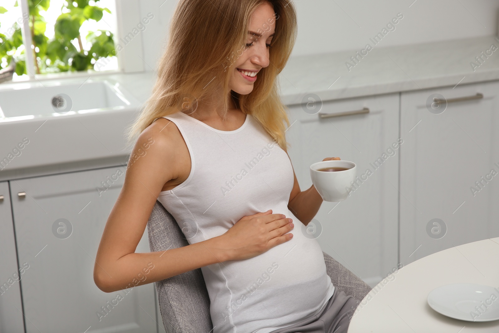 Photo of Beautiful pregnant woman drinking tea in kitchen