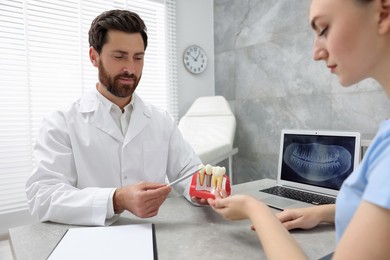 Photo of Doctor showing patient educational model of dental implant in clinic