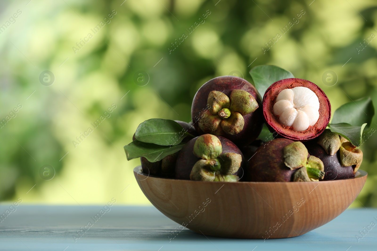 Photo of Delicious tropical mangosteen fruits on light blue table. Space for text