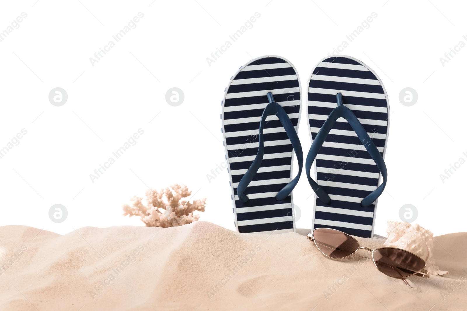Photo of Striped flip flops, coral, sea shell and sunglasses on sand against white background